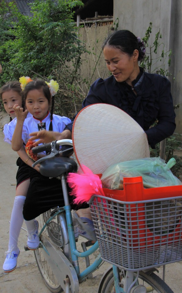 Una mamma in bici con le sue gemelle vestite a festa